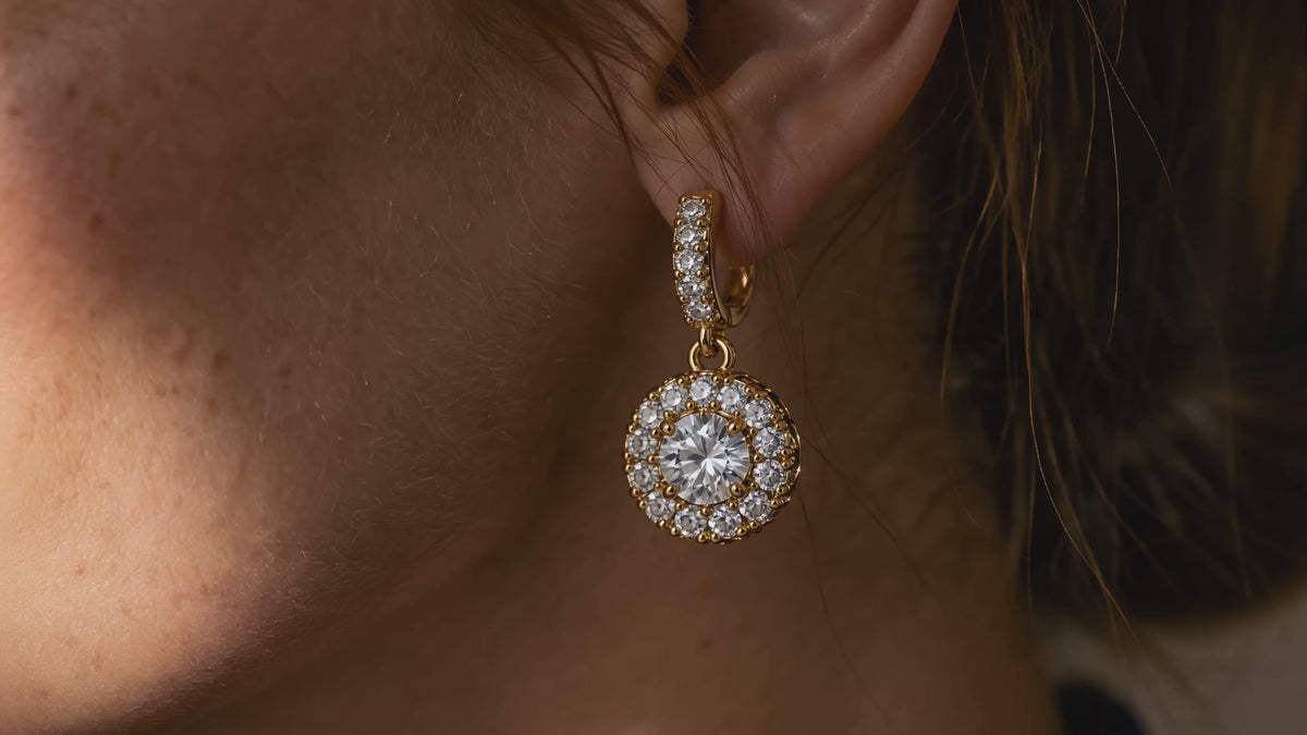 Gold-tone crystal halo drop earrings shown in close-up, worn by an AI-generated adult model, and displayed as a pair.