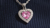 Silver-tone pink crystal heart pendant shown in close-up, worn by an AI-generated adult model, and displayed on ivory stone.