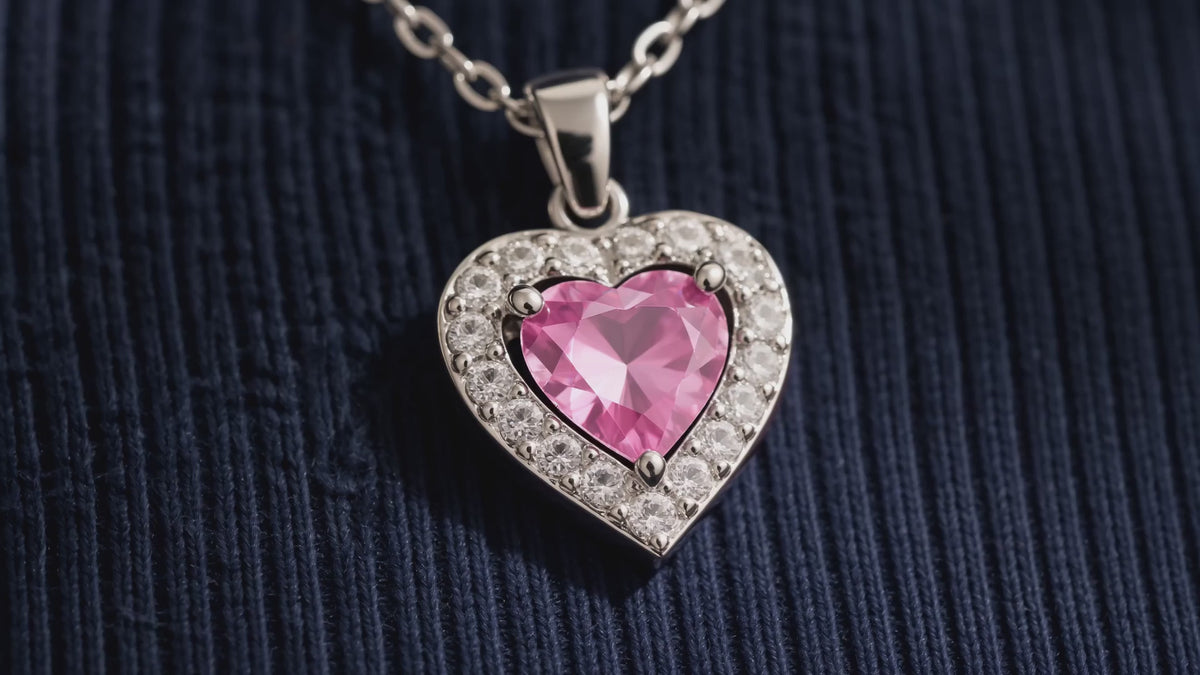 Silver-tone pink crystal heart pendant shown in close-up, worn by an AI-generated adult model, and displayed on ivory stone.